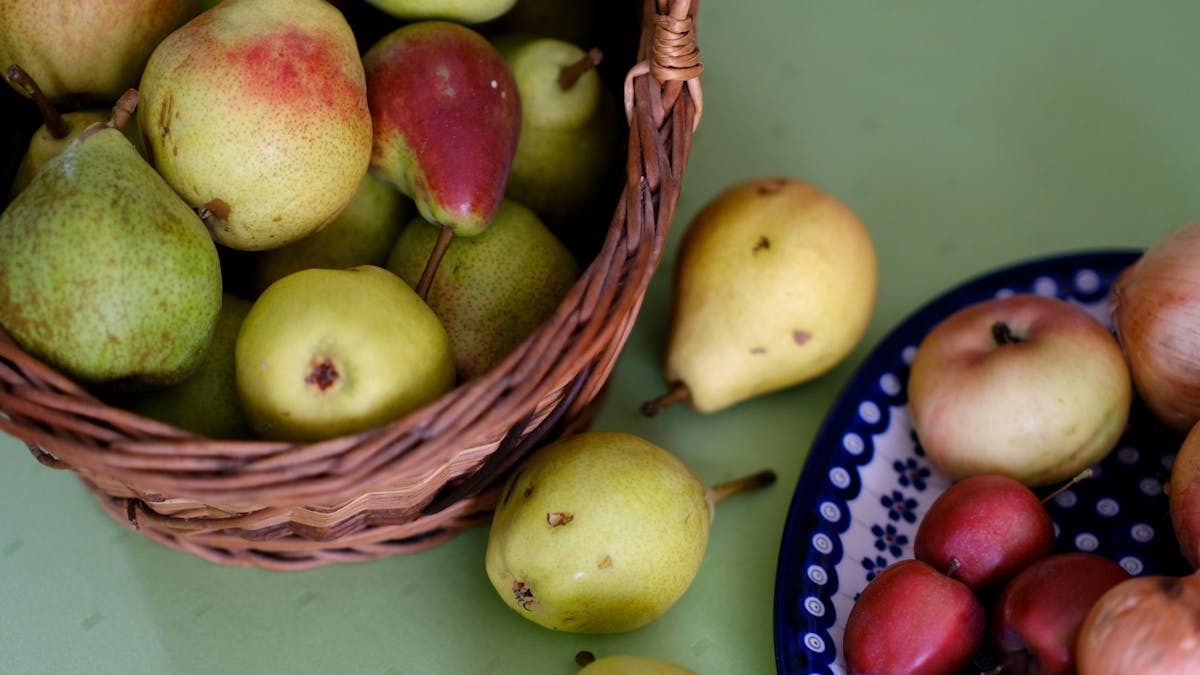 A vibrant assortment of pears and apples in a woven basket and ceramic plate, showcasing freshness.