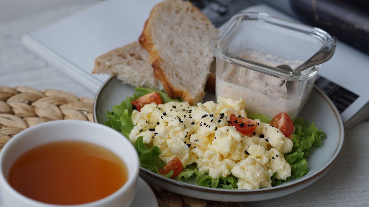 A delicious breakfast with scrambled eggs, bread, and tea on a cozy table setting.